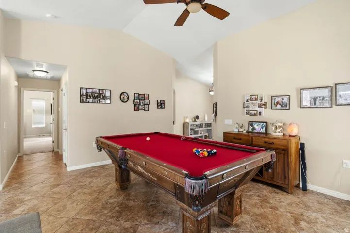 Spacious entertainment area featuring vaulted ceilings, a ceiling fan with integrated lighting, and tile flooring