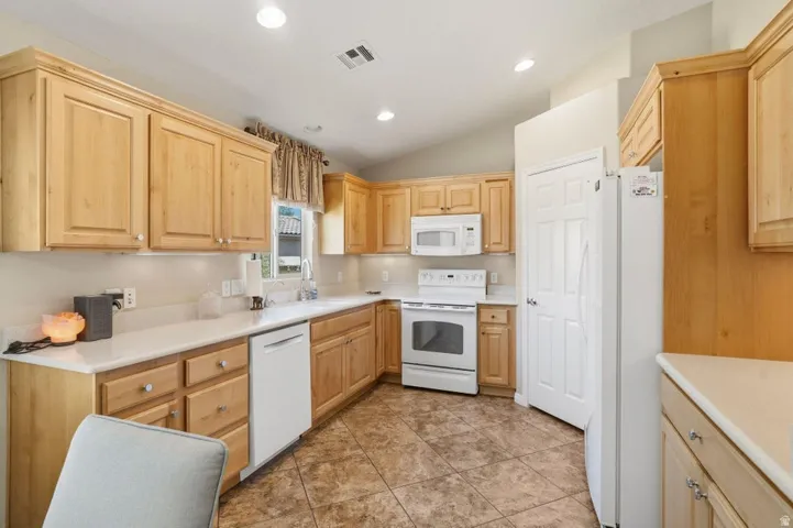 Kitchen featuring light wood cabinetry, white countertops, white appliances, and tiled flooring