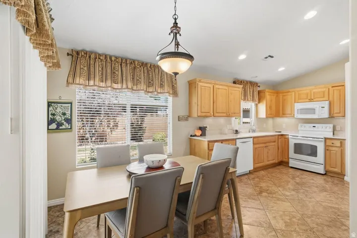Spacious kitchen with a dining area, featuring wood cabinetry, white countertops, white appliances, and tiled flooring