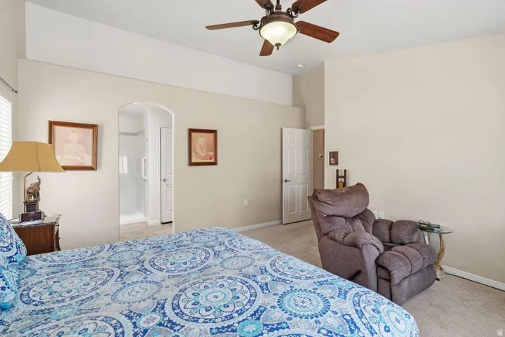 Carpeted room featuring vaulted ceilings, a ceiling fan with integrated lighting, an arched doorway, and an interior door