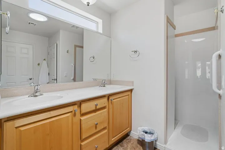 Bathroom featuring a double vanity with light wood cabinetry, a light-toned countertop, and dual integrated sinks