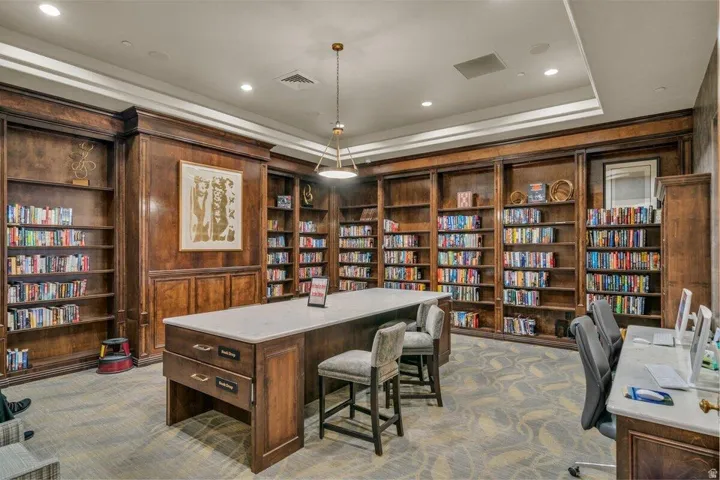 Library featuring extensive built-in wooden shelving, a large central island with a light-toned countertop, recessed lighting, and patterned carpeting