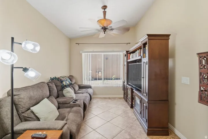 Vaulted ceiling with a ceiling fan, window with vertical blinds, tile flooring, and a built-in media cabinet