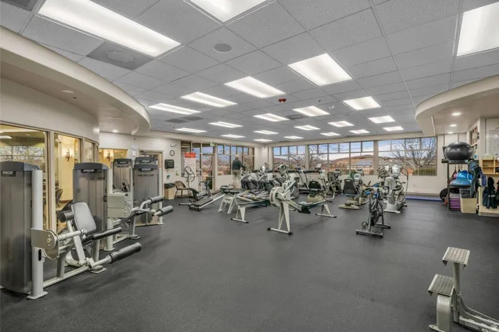 Fitness center with rubber flooring, extensive exercise equipment, abundant natural light, recessed ceiling lights, and large windows