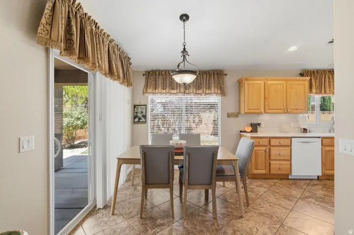 Dining area featuring tile flooring, a sliding glass door to the exterior, and a built-in kitchen with light wood cabinetry and a white dishwasher