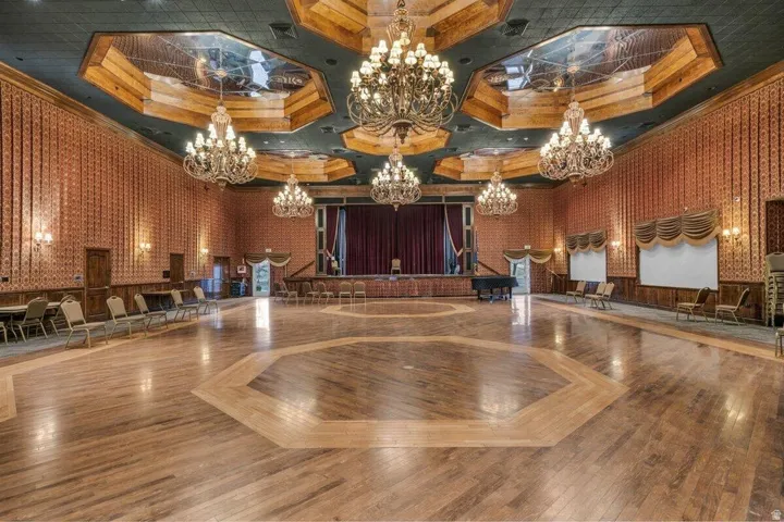 Expansive event space featuring a stage with red curtains, patterned wall coverings, and multiple ornate chandeliers