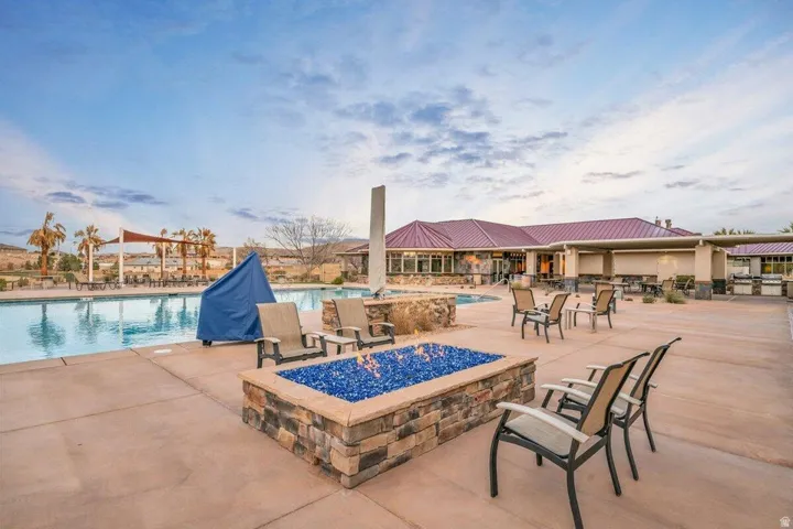 Expansive outdoor amenity area featuring a large swimming pool, a stone-clad fire pit with blue glass accents, and a recreational building with a red roof