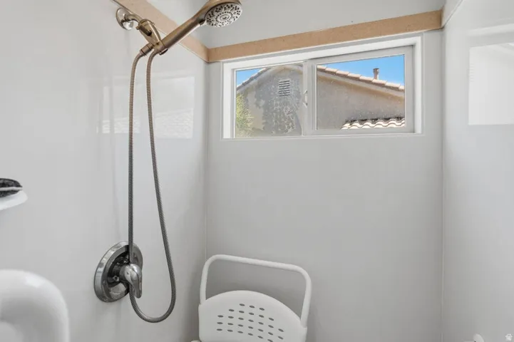 Shower enclosure featuring a bronze-finish showerhead, a single-handle chrome-finish control, white paneling, and a horizontal sliding window