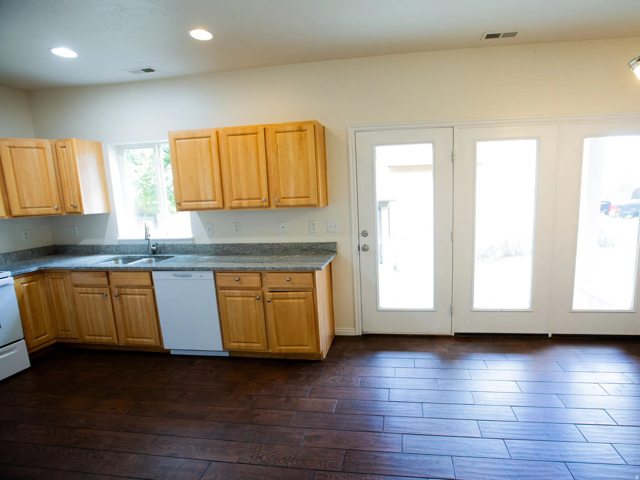 Kitchen featuring wood-finish flooring, light wood cabinetry, granite-style countertops, and a double-basin sink with a window overhead