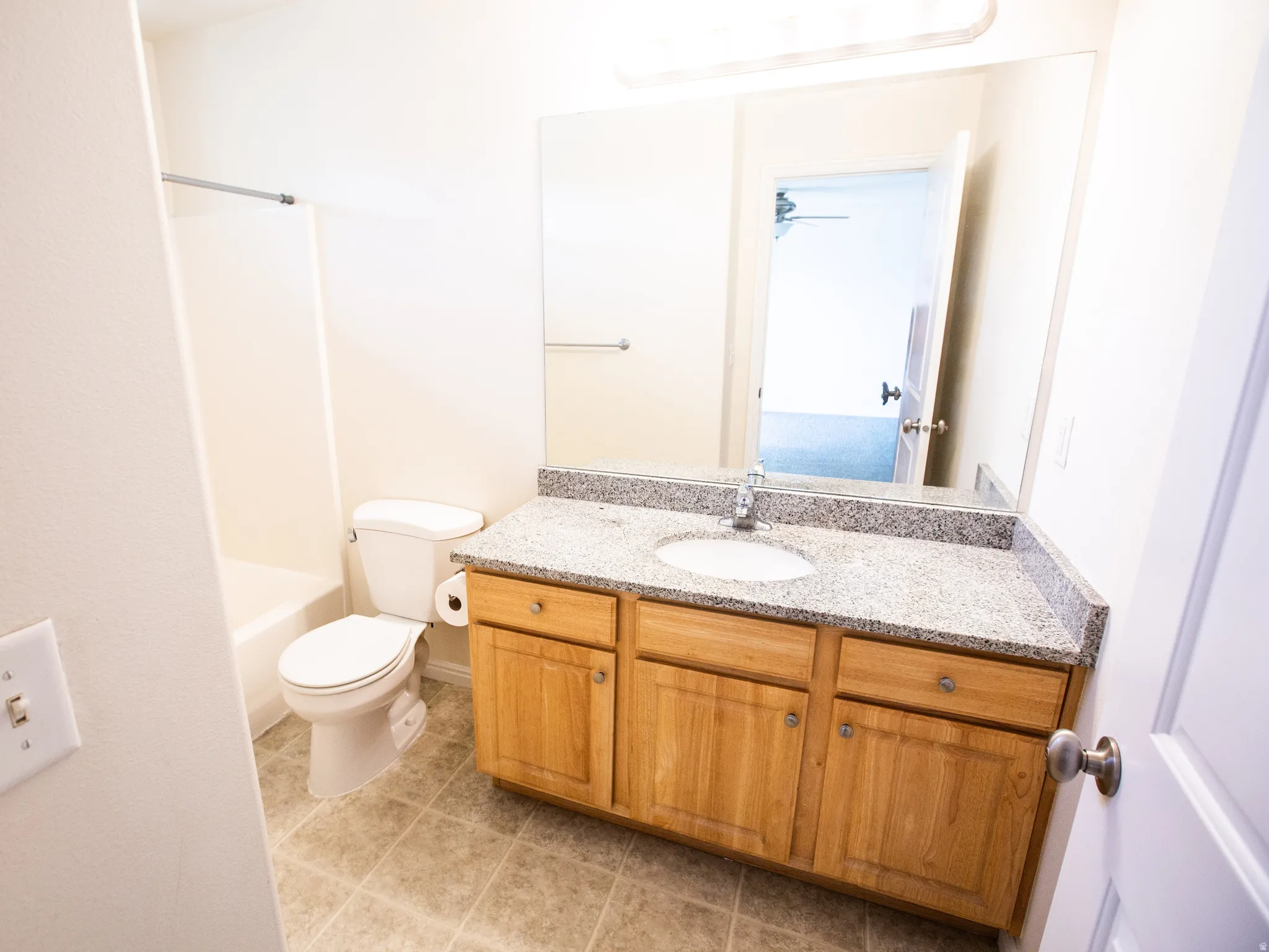 Bathroom featuring a light wood-finish vanity with a speckled countertop, an integrated sink, and a large wall-mounted mirror