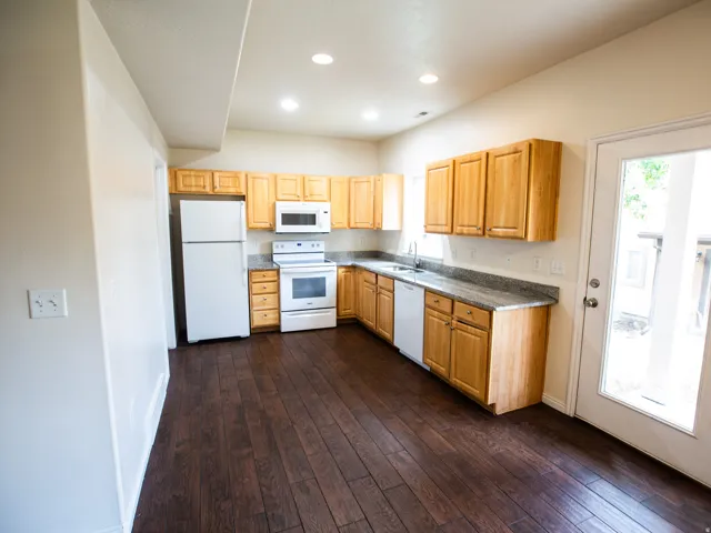 Kitchen featuring wood-finish flooring, light wood cabinetry, white appliances, speckled countertops, and recessed lighting