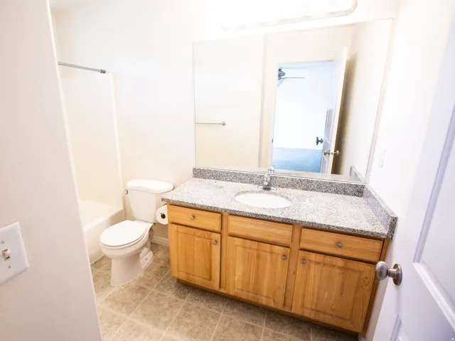 Bathroom featuring a light wood-finish vanity with a speckled countertop, an integrated sink, and a large wall-mounted mirror