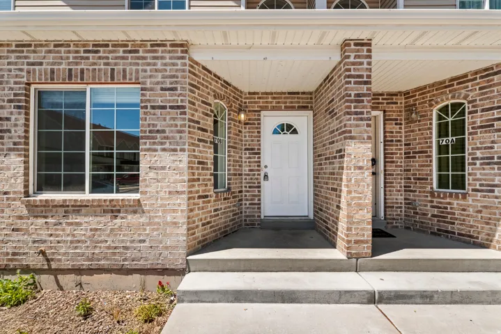 Brick exterior featuring a covered porch, white entry door with an arched window, arched side windows, a large paneled window, and concrete steps