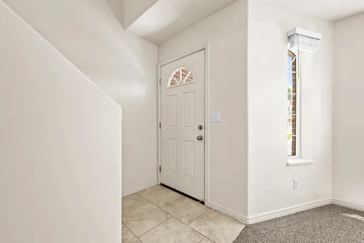 Entryway featuring a white door with an arched window insert, tiled flooring, and a tall arched window with a window sill