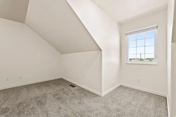 Attic room featuring a single window with gridded panes, light gray carpeting, neutral wall paint, white baseboards, and sloped ceiling details