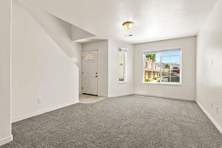 Spacious living area featuring neutral-toned carpeting and light-colored walls