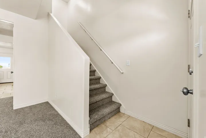 Carpeted staircase with a white handrail, complemented by neutral wall finishes and white baseboards