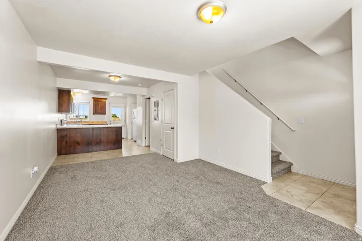 Open-concept living area featuring light gray carpeting, neutral wall paint, and a staircase with a white handrail