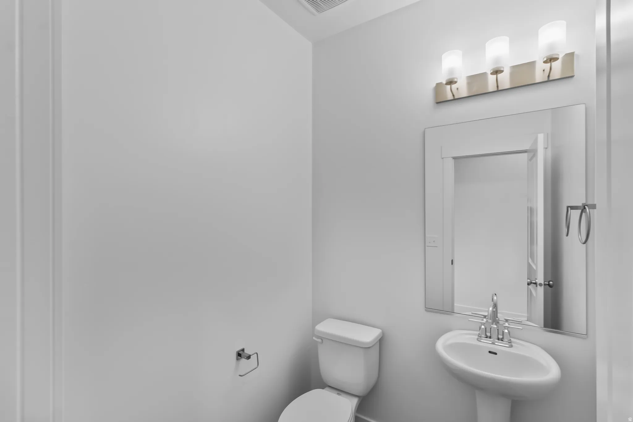 White pedestal sink with chrome faucet, framed mirror, and a three-light vanity fixture featuring brushed nickel and frosted glass