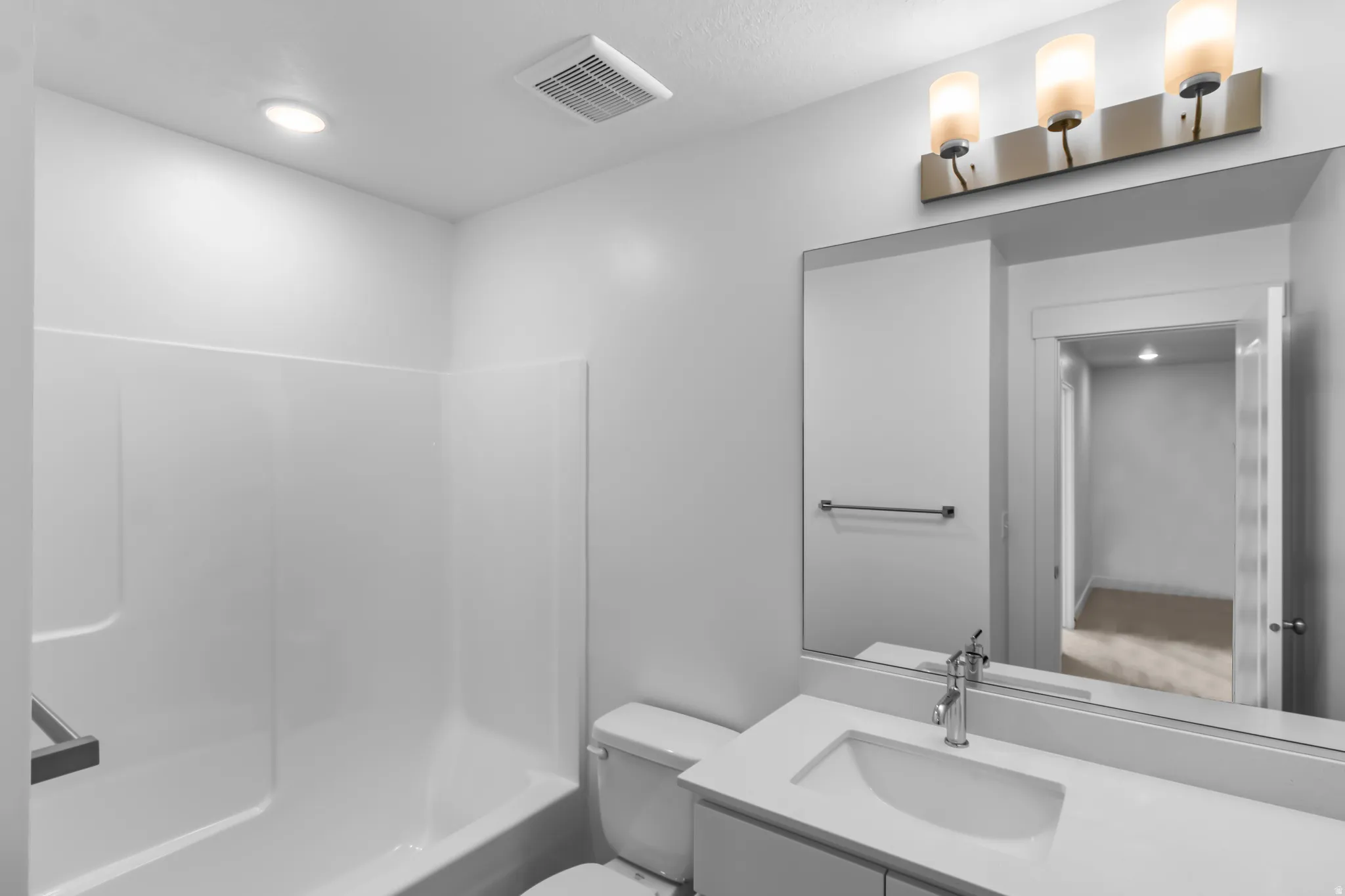 Bathroom featuring a white integrated sink vanity with a chrome faucet, a large frameless mirror, and a three-light vanity fixture