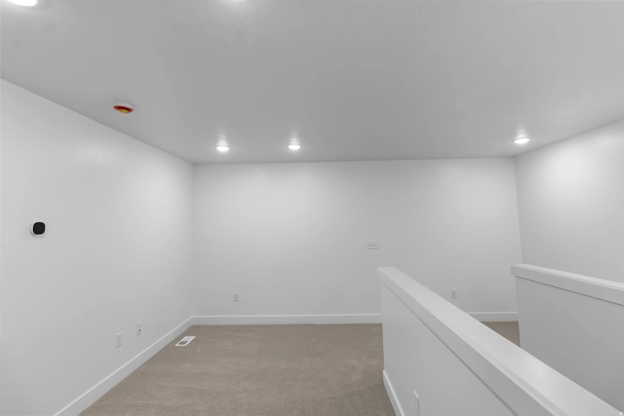 Carpeted room with white walls, recessed ceiling lighting, and a white railing