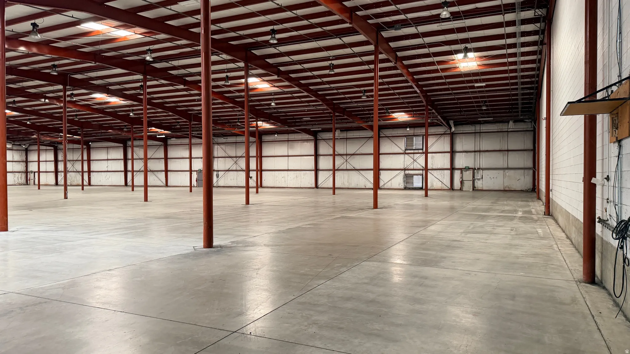 Expansive warehouse space featuring a polished concrete floor, exposed red structural beams, and corrugated metal walls