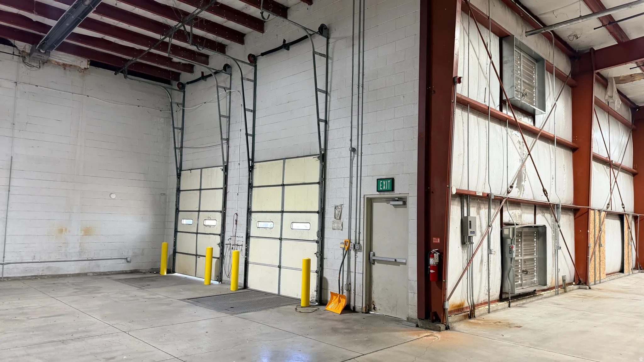 Spacious interior with two overhead truck dock doors featuring translucent panels, concrete flooring, exposed industrial ceiling, and a side exit door