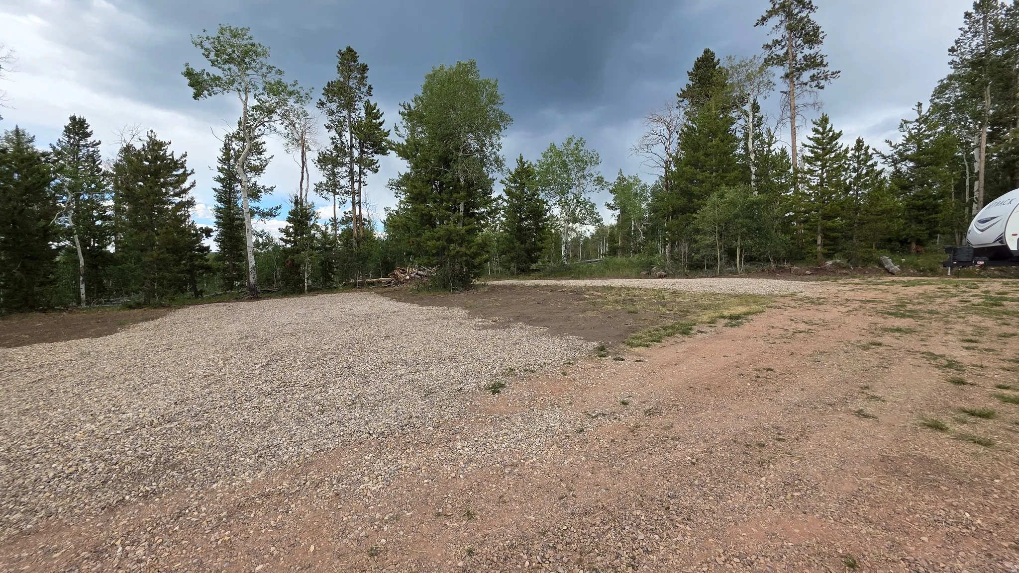 Spacious gravel and dirt lot surrounded by mature evergreen and deciduous trees