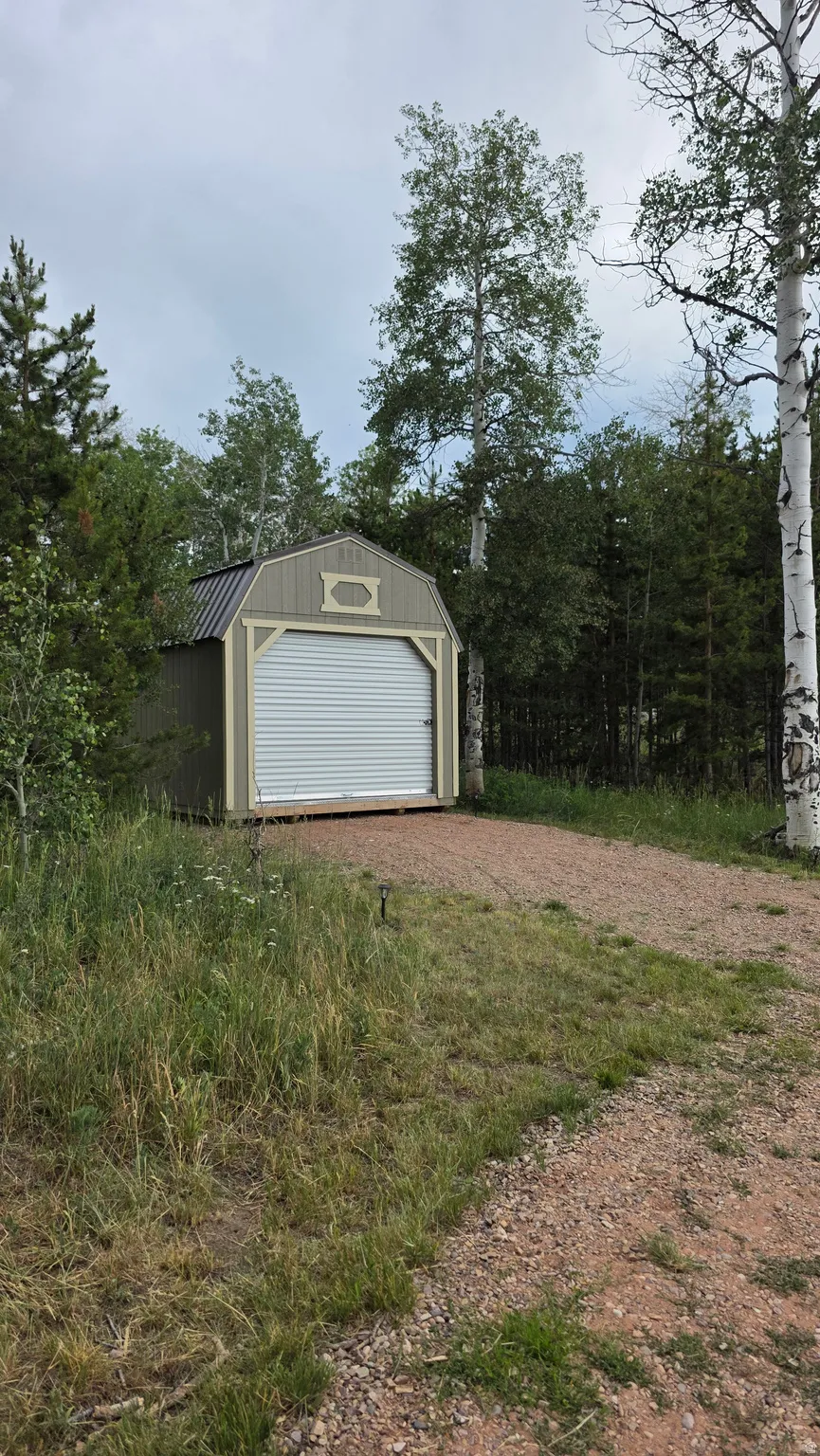 Detached shed with a light green exterior and white trim, featuring a roll-up door