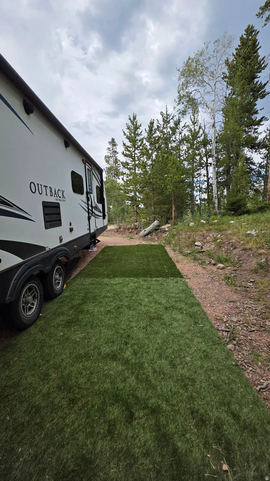Artificial turf pad beside a parked trailer, with a natural treeline in the background