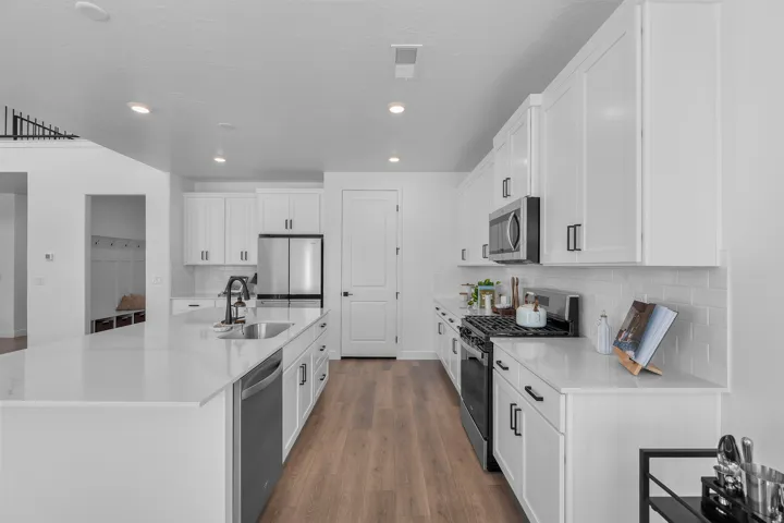 Modern kitchen featuring white cabinetry, light countertops, wood-finish flooring, stainless steel appliances, and an expansive island with an undermount sink