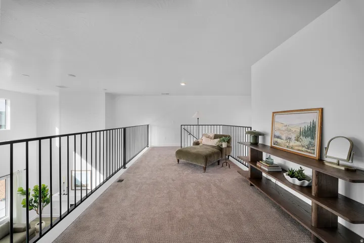 Upper-level loft space featuring neutral carpet flooring and a black metal railing overlooking a lower level