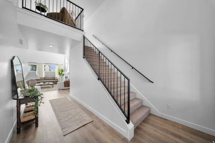 Entryway featuring wood-finish flooring, a carpeted staircase with black metal railings, and a white wall finish