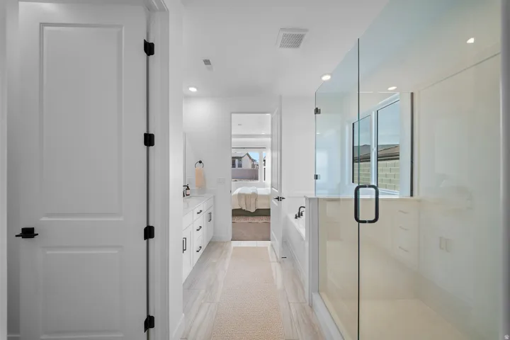 Sleek bathroom featuring a glass-enclosed shower, a built-in tub, a double vanity with white cabinetry, and light-toned tile flooring
