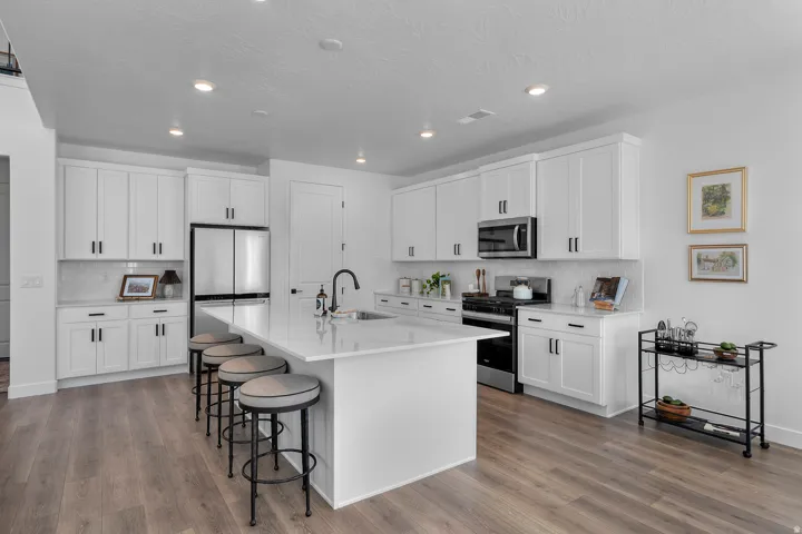Kitchen featuring a large central island with seating, white shaker-style cabinetry with dark hardware, stainless steel appliances, recessed lighting, and wood-finish flooring