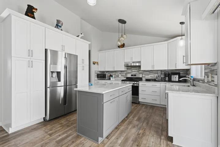 Modern kitchen featuring white cabinetry, a central island with a grey base, wood-finish flooring, stainless steel appliances, and a mosaic tile backsplash