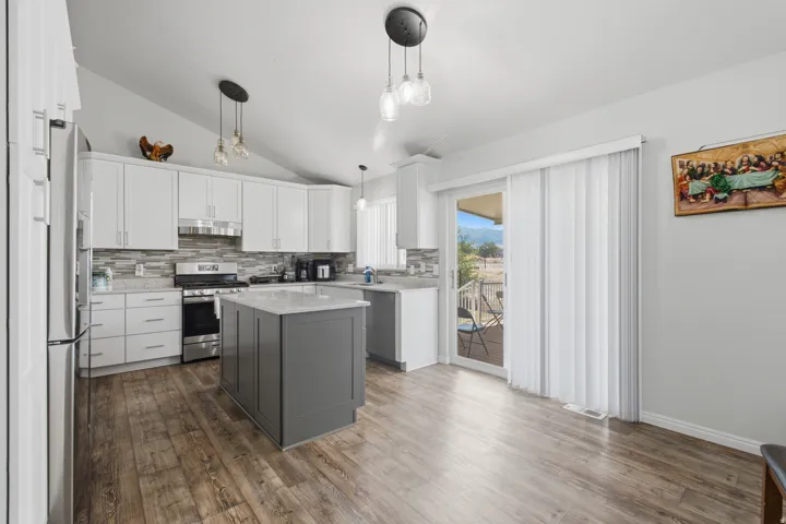 Modern kitchen featuring white cabinetry, a contrasting gray island with a light-colored countertop, stainless steel appliances, and wood-finish flooring