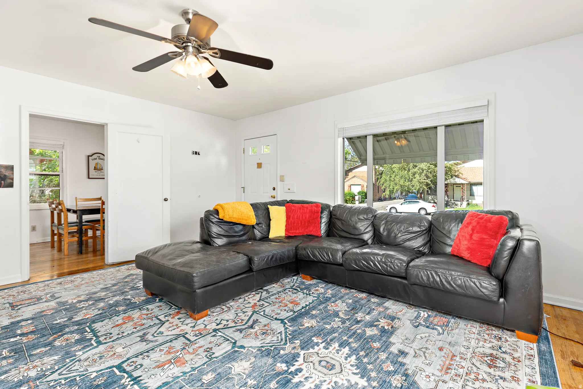 Living area featuring light wood-finish flooring, a ceiling fan with light fixture, and a large window