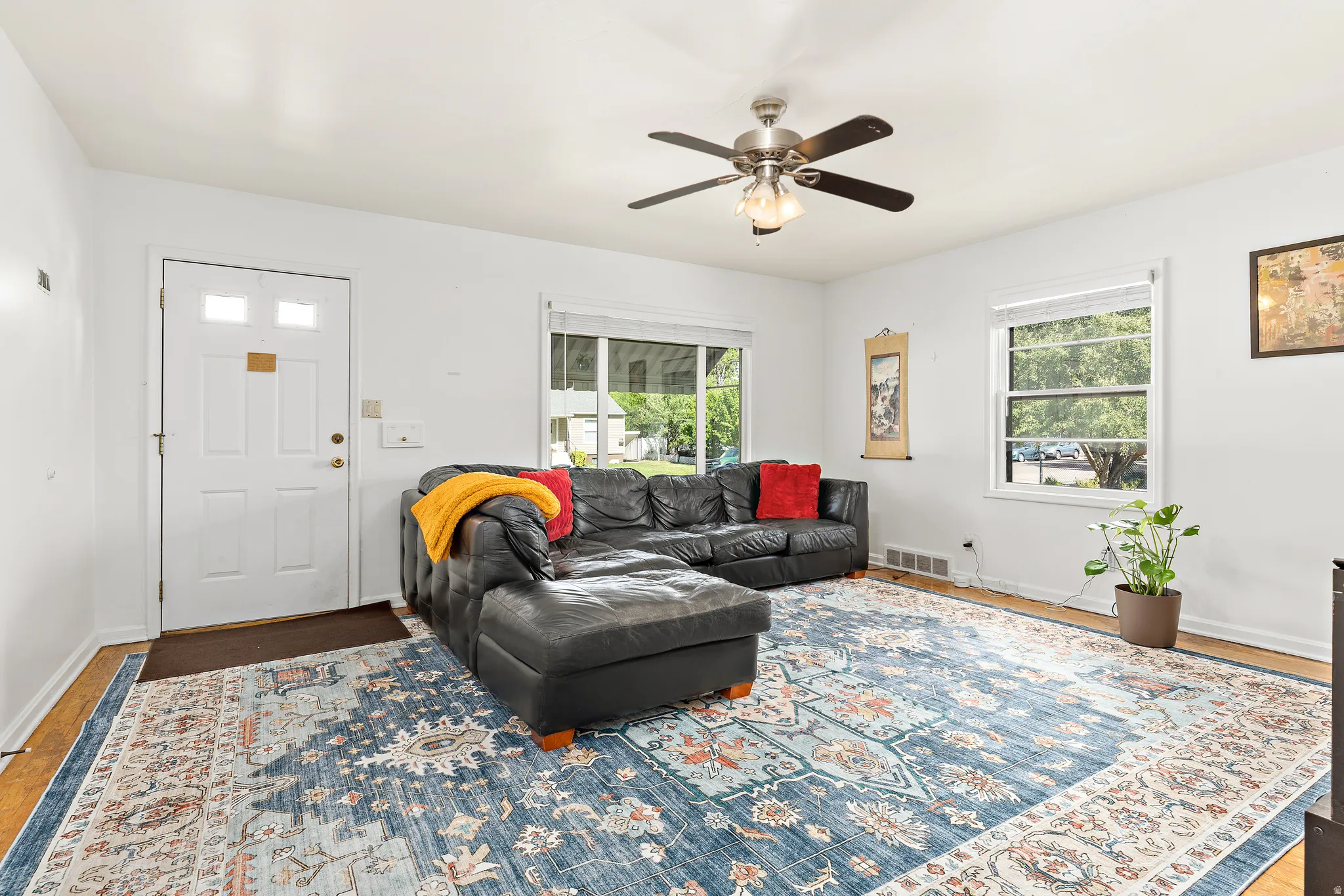 Bright living area featuring white walls, wood-finish flooring, a ceiling fan with integrated lighting, and multiple windows