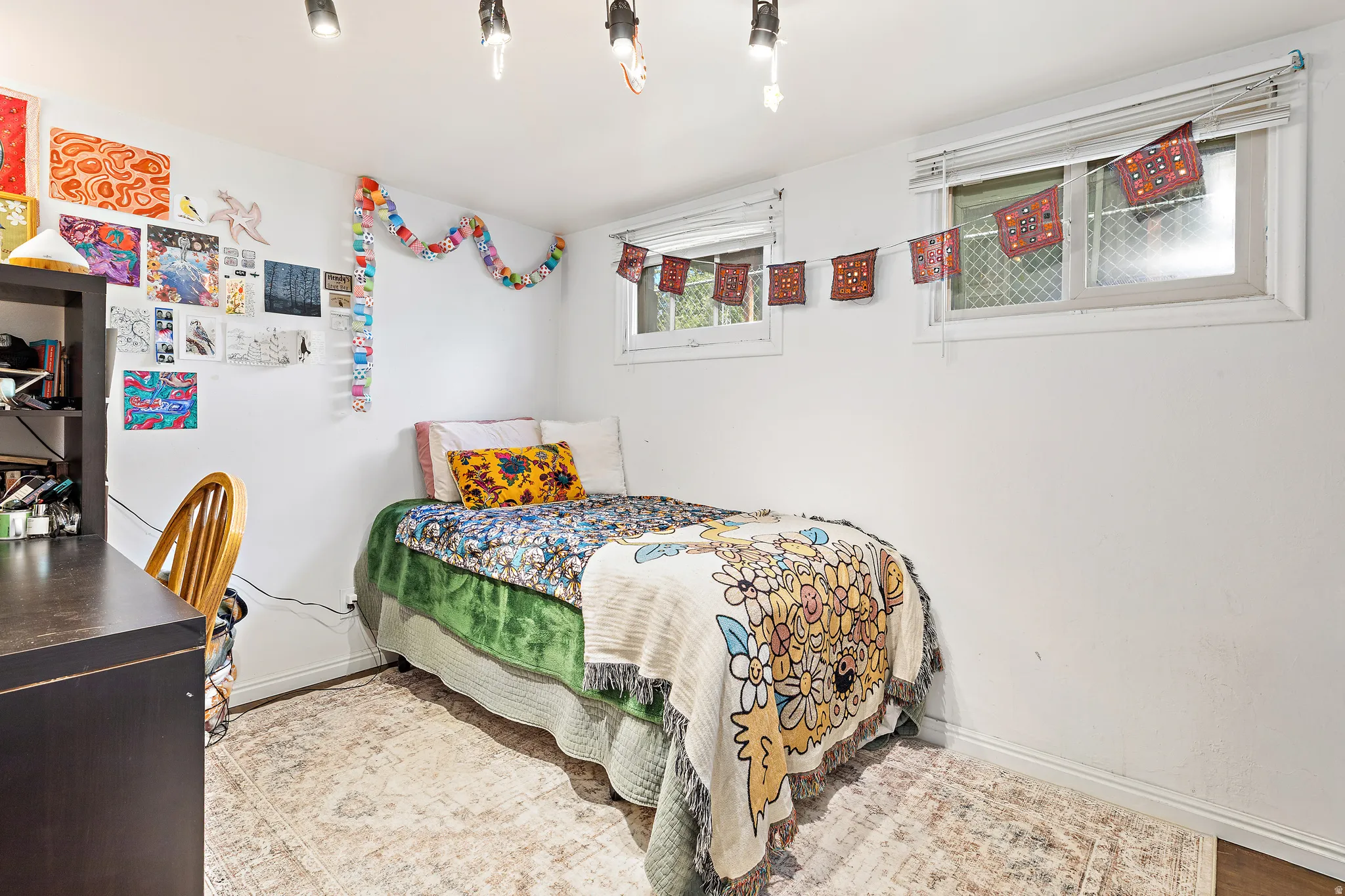 White walls featuring two windows with white blinds, track lighting, and wood-finish flooring partially covered by an area rug