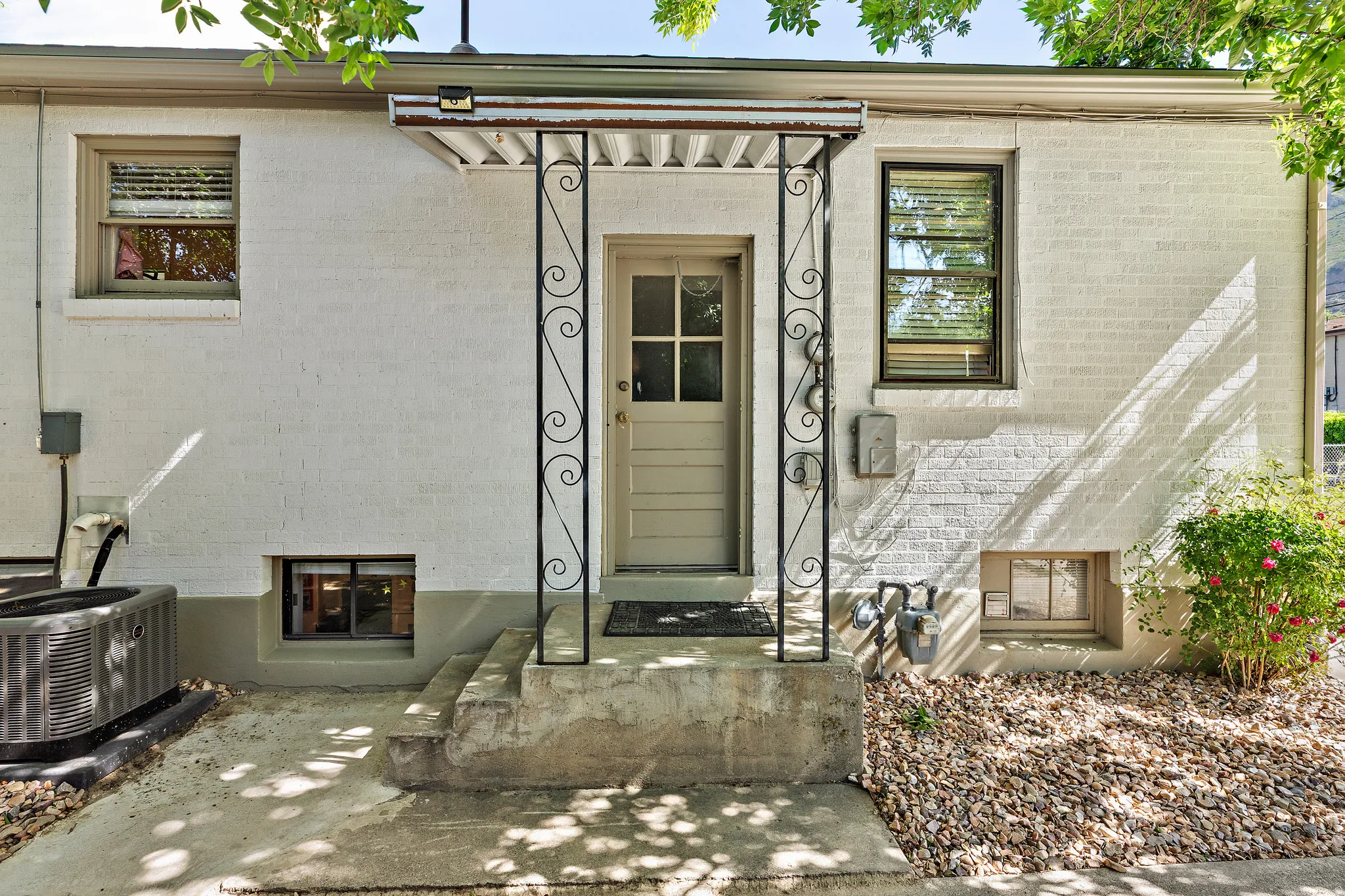 White brick exterior featuring a covered entry with decorative wrought iron supports