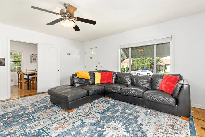 Living area featuring light wood-finish flooring, a ceiling fan with light fixture, and a large window