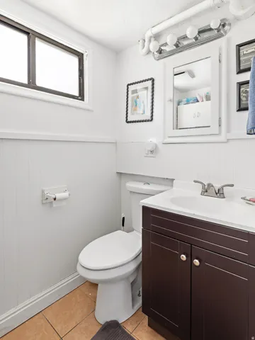 Bathroom featuring a vanity with a white countertop and dark wood-finish cabinetry, a white toilet, and light brown floor tiling