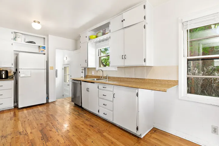 Kitchen featuring wood-finish flooring, white cabinetry, a stainless steel dishwasher, and a double-basin sink