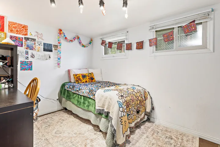 White walls featuring two windows with white blinds, track lighting, and wood-finish flooring partially covered by an area rug