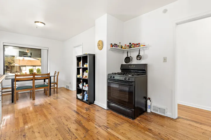 Hardwood flooring throughout a dining area with a large window and a kitchen area featuring a black gas range