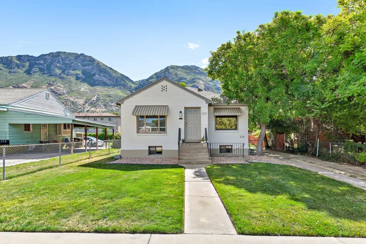 Stucco exterior residence featuring a front lawn, concrete pathway, and mature shade tree