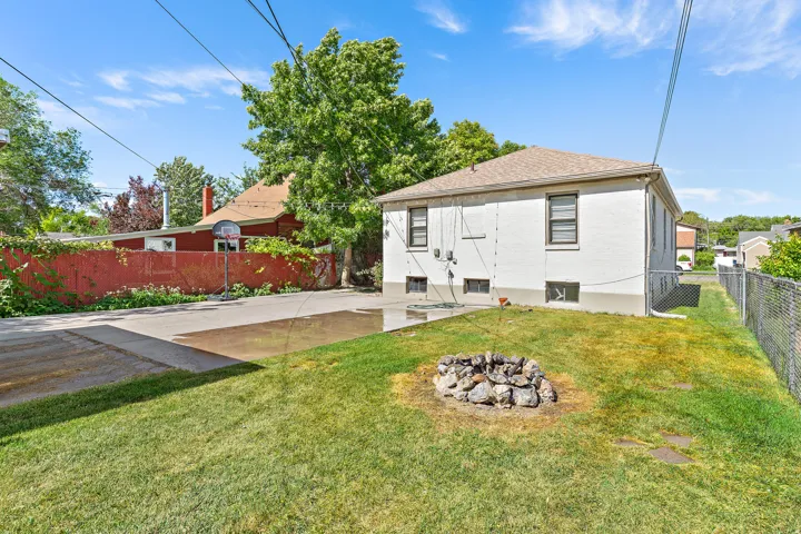 Expansive backyard featuring a lush lawn, stone fire pit, and a paved patio area