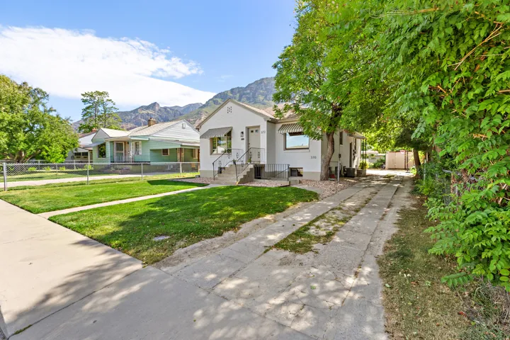 White exterior residence featuring a front lawn, mature trees, concrete driveway, and a partially covered front porch