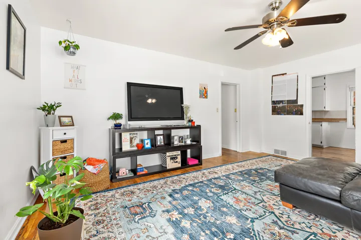 Bright living area featuring wood-finish flooring, a ceiling fan with integrated lighting, and white walls